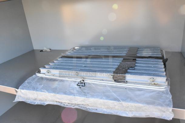 Brand new shelving unit with visible scratches and dents, metal shelves stacked and secured with tape, plastic wrap partially covering.