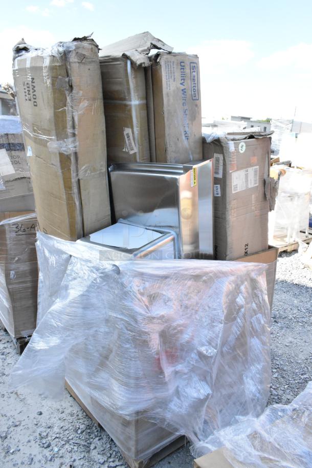 Stack of unopened items, including a wok range and stainless work table, in original packaging with some damage.