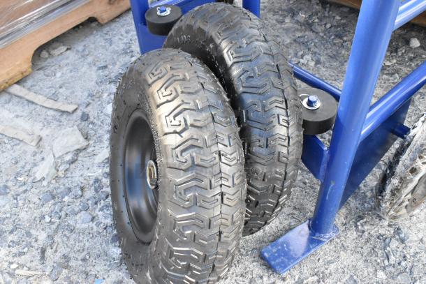 Brand new blue metal barrel dolly with two large black wheels, slight scratches visible, durable for heavy loads.