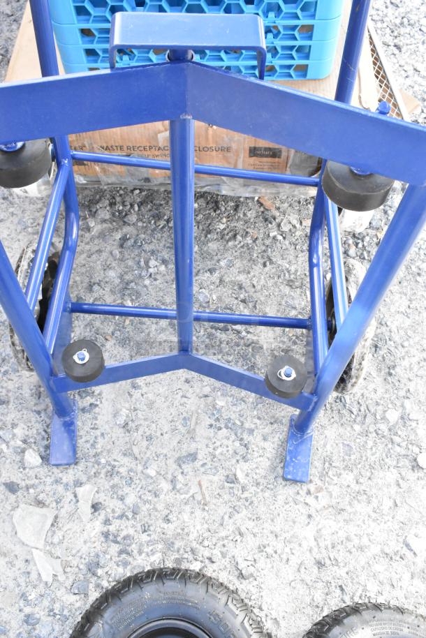 Blue metal barrel dolly, brand new with minor scratches and dents, featuring robust frame and solid wheels.