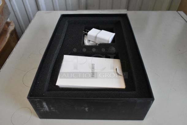 Box containing tablet accessories including a Samsung manual and charger, indicating possible model or brand.