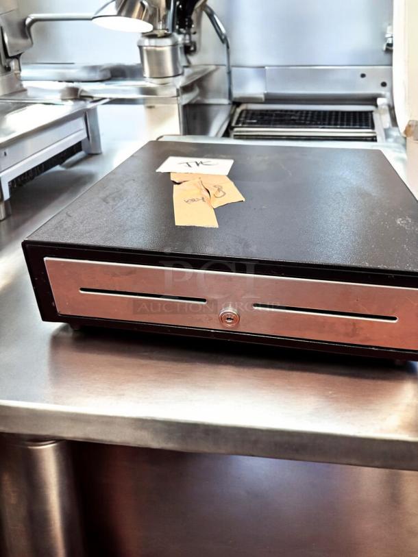 APG Cash Drawer VBS579-BL1616 in excellent condition on metal counter. Includes lock and paper tags with "key" text.
