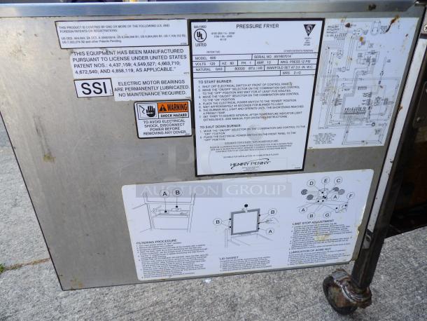 Henny Penny 600 stainless steel pressure fryer in excellent condition, natural gas-powered, on commercial casters, 80,000 BTU. Labels and schematics visible.