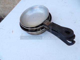 Set of three 7" commercial frying pans with rubber grips, showing visible wear, stacked on a white surface.