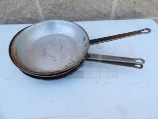 Three 10" commercial frying pans with metal handles, showing wear, indicating durability and value for frequent use.