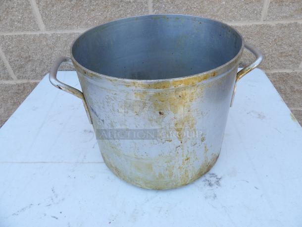 24 Qt. aluminum stock pot with handles, showing signs of use and tarnishing, placed on a white surface.