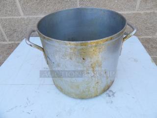 24 Qt. aluminum stock pot with handles, showing signs of use and tarnishing, placed on a white surface.