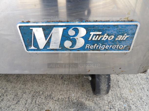 Turbo Air MST-60 refrigerator badge, blue background, "M3 Turbo Air Refrigerator" text. Wheel visible below. Slight wear.