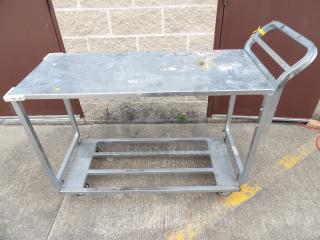18" x 52" two-shelf chrome heavy-duty utility cart with visible wear. Features handle and caster wheels for mobility.