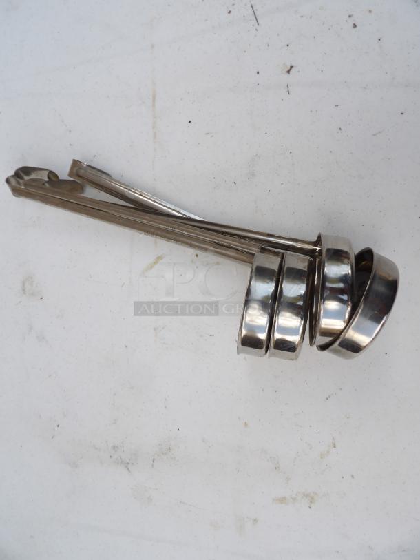 Set of four 6-ounce stainless steel ladles, used condition, stacked together, suitable for liquid serving in kitchens.