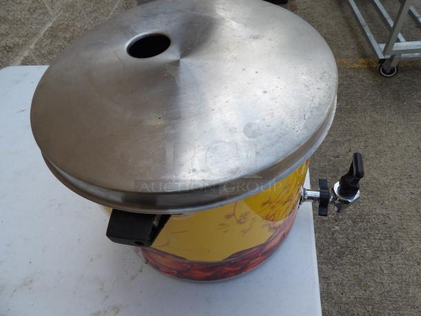 Stainless steel tea dispenser with lid and spigot, showing signs of use. Suitable for beverages.