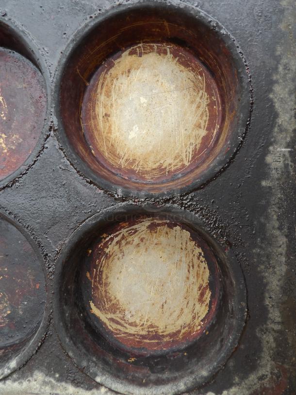 Worn pot pie pan with multiple 5-inch round molds, visible scratches, and patina on the surface, indicating vintage condition.