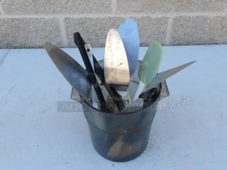 Miscellaneous pie spatulas in a metal container, various sizes and conditions, suitable for kitchen use.