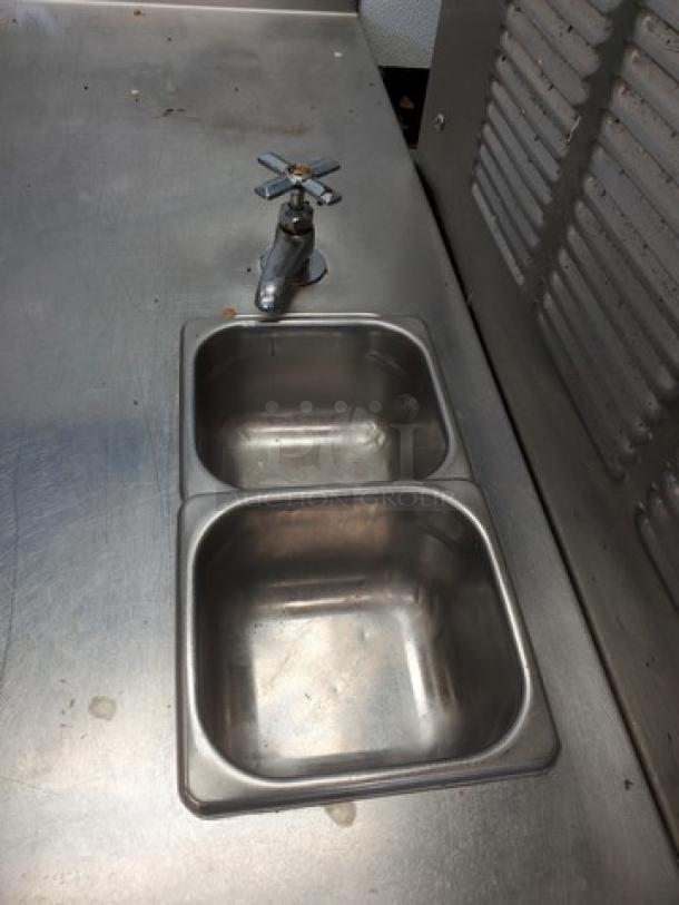 Stainless steel work station with dual sinks and faucet. Durable surface with minor wear, ideal for commercial kitchens.