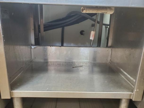 Stainless steel work station with open storage, visible pipes, and a sturdy surface. Good condition, ideal for kitchen use.
