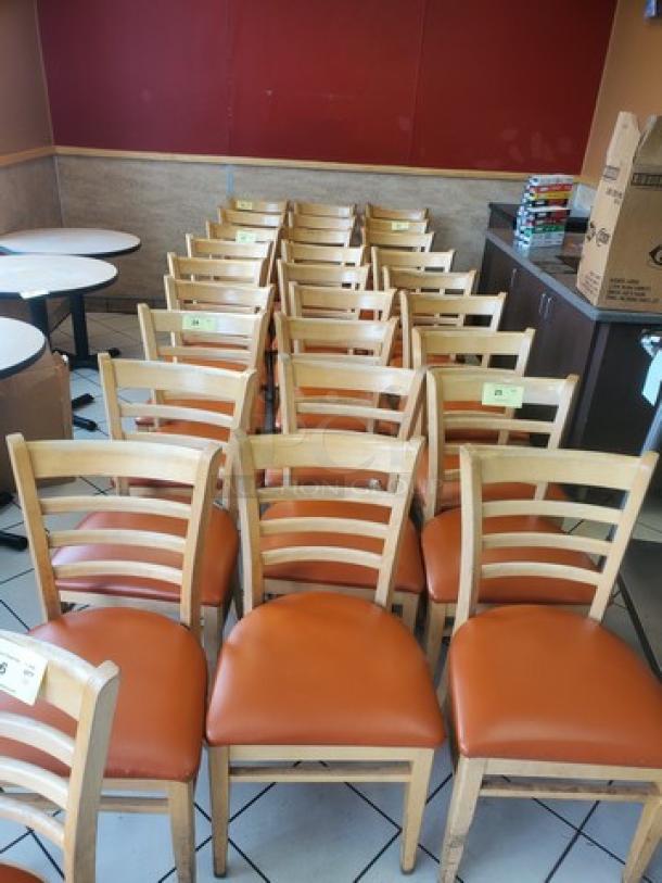 Lot of 4 wooden chairs with orange cushioned seats. Light wood finish, ladder-back design. Ideal for dining or casual settings.