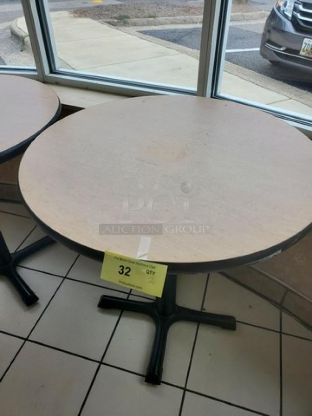 Lot of 2 round table tops with bases, light wood finish, black metal pedestal. Includes tag "32 QTY 2." Signs of use.