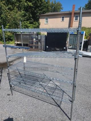 4 Tier wire shelf, metal construction, outdoor setting, adjustable shelves, minor wear, perfect for storage and organization.