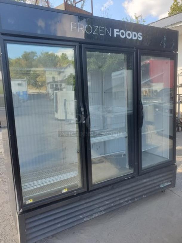 True GDM-72F-HC-TSL01 78" 3-section glass-door merchandiser freezer, black frame, labeled "FROZEN FOODS," outdoor setting.