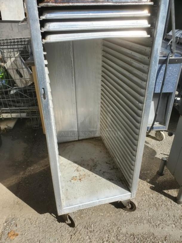 Mobile sheet pan rack, metal, on wheels, upright, empty slots, visible wear, suitable for commercial kitchen use.