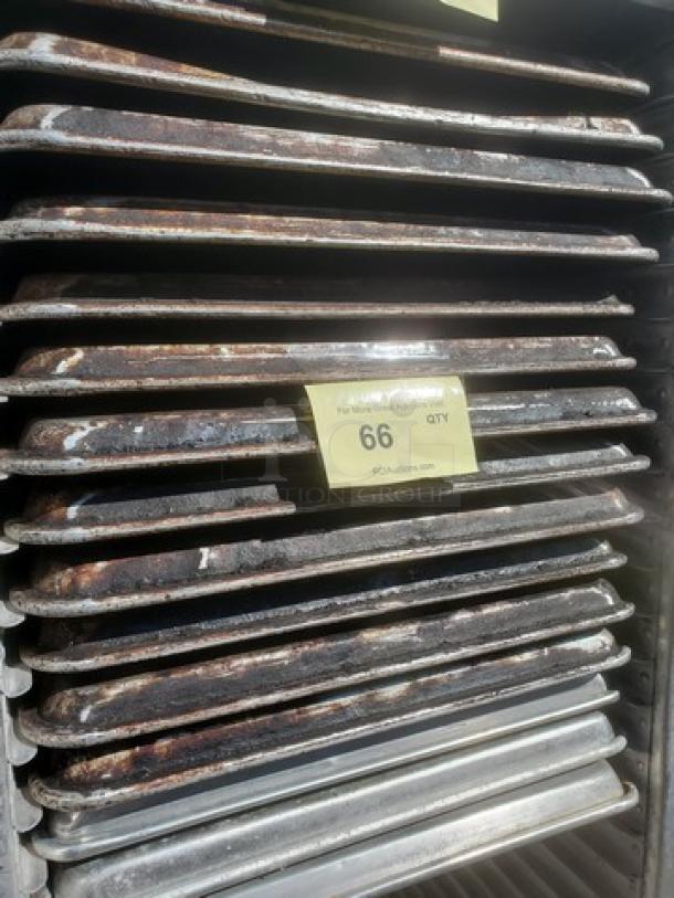 Lot of 15 sheet pans with visible wear, stacked together. Tag reads "66 QTY" indicating quantity or lot number.