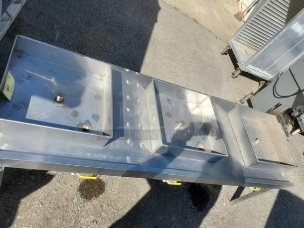 Three-compartment stainless steel sink with drainboards, slight wear, visible mounting and drainage fixtures, tags with lot number.