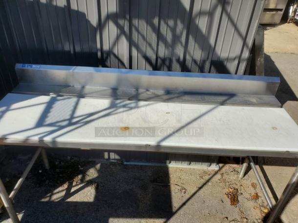 Stainless steel work counter with backsplash, used condition, showing minor rust spots, sturdy metal legs, ideal for kitchen or workshop use.