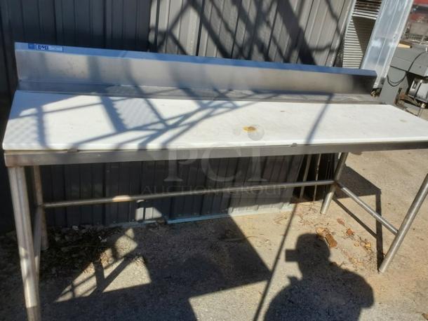 Stainless steel work counter with backsplash, sturdy legs, and scuff marks; ideal for kitchen or industrial use.