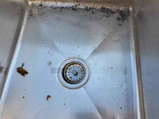 Stainless steel sink with three compartments, visible stains and debris. Durable material, ideal for commercial kitchen use.