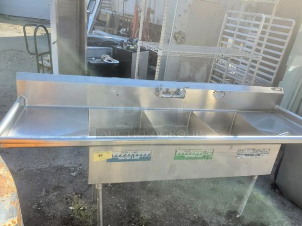 3 compartment stainless steel sink, used condition, with visible wear and bolt marks. Labels indicate model and capacity.