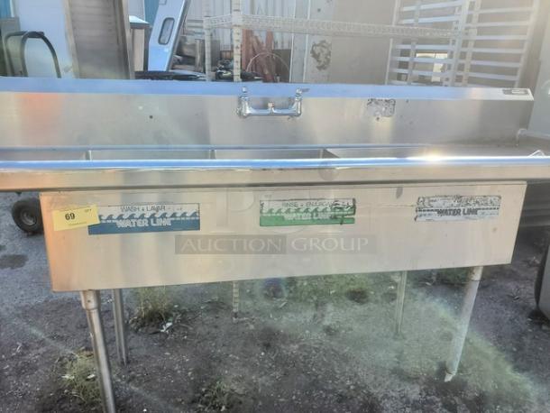 3 compartment stainless steel sink with attached faucets. Visible wear and labels indicating wash, rinse, sanitize sections.