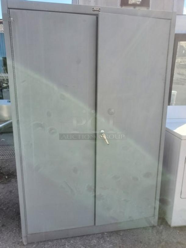Gray metal cabinet with two doors and a key lock, in used condition. Perfect for secure storage.