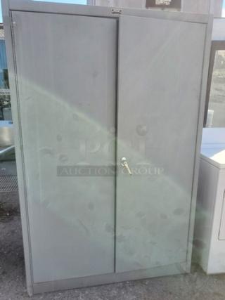Gray metal cabinet with two doors and a key lock, in used condition. Perfect for secure storage.