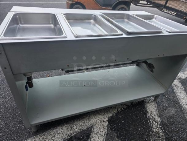 4-well propane steam table in metal, used condition, with visible valves and storage shelf, ideal for catering or restaurant use.