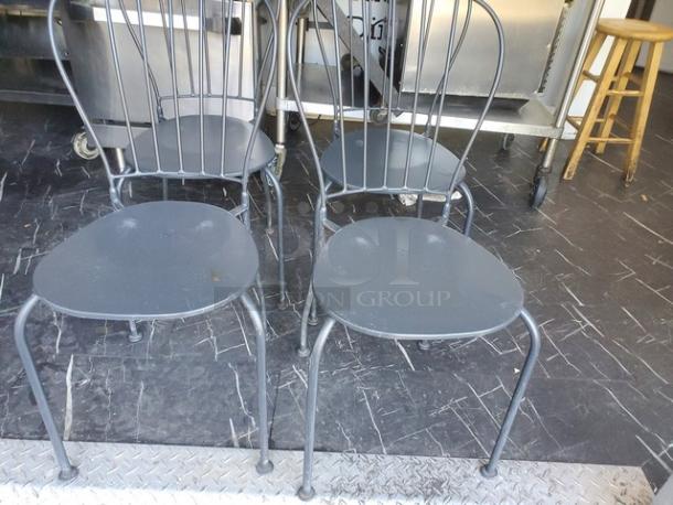 Lot of 4 black patio chairs with metal frames and curved backs, in used condition. Ideal for outdoor seating areas.