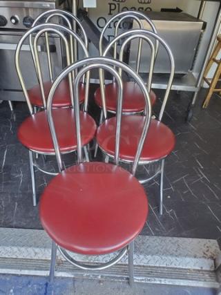 Lot of 4 red cushioned dining chairs with metal frames, gently used. Circular seats, arched backs, and sturdy construction.