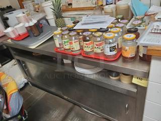 Stainless steel work counter with lower storage, in used condition. Contents on top such as jars, dishes, and papers not included.