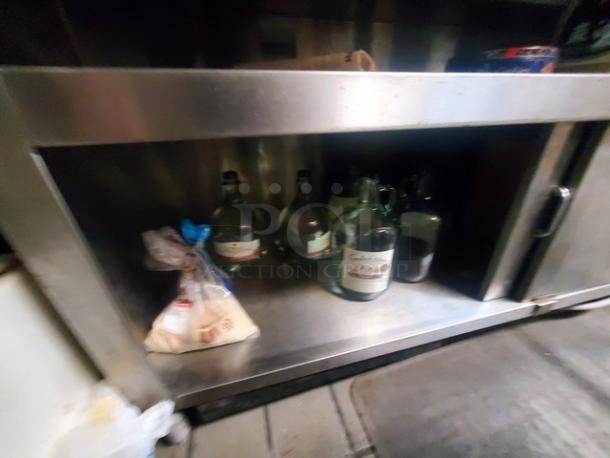 Stainless steel work counter with sliding doors, minor surface wear, items inside not included. Durable kitchen utility.