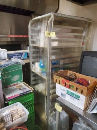 Stainless steel sheet pan rack with multiple shelves, used condition, clear cover, tag marked "112." Contents not included.