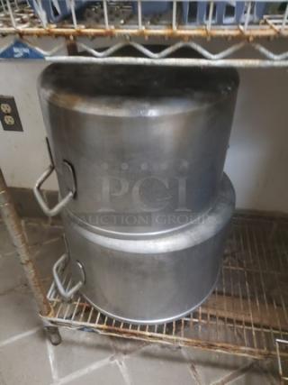 Lot of 2 large metal pots with handles, signs of wear, on a wire shelf. Ideal for bulk cooking or commercial use.