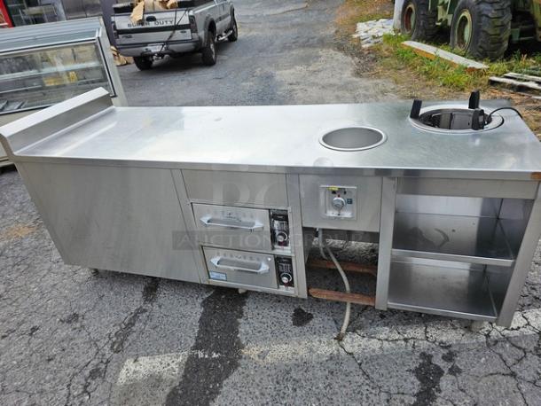 Custom stainless steel work counter and warmer with integrated round heating element, storage shelves, and dual control panels.
