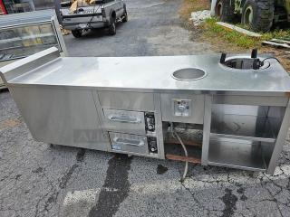 Custom stainless steel work counter and warmer with integrated round heating element, storage shelves, and dual control panels.