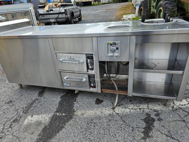 Custom stainless steel work counter and warmer with dual drawers, control panel, and open shelving. Ideal for commercial use.