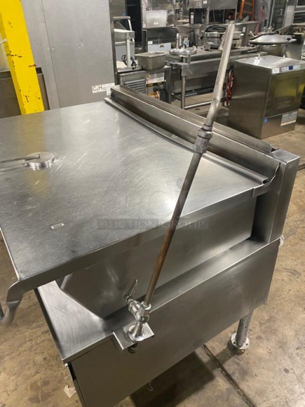 Commercial stainless steel electric braising pan with tilt feature and swivel faucet, mounted on legs; industrial kitchen setting.