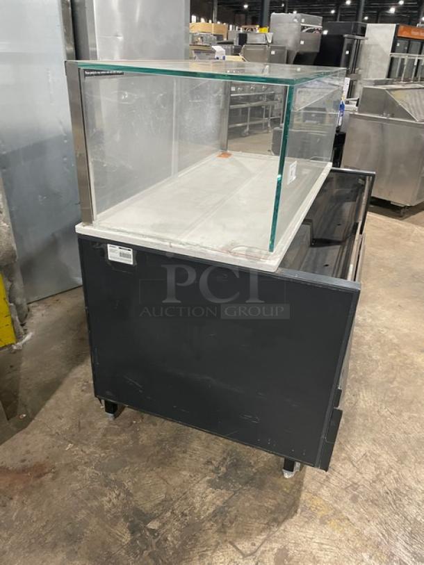 Structural Concepts black multi-level refrigerated display case, with top enclosed glass showcase, on legs, visible markings.