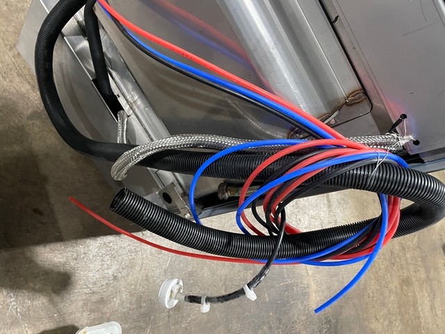 Rear of undercounter dishwasher showing water and chemical dispenser line connections