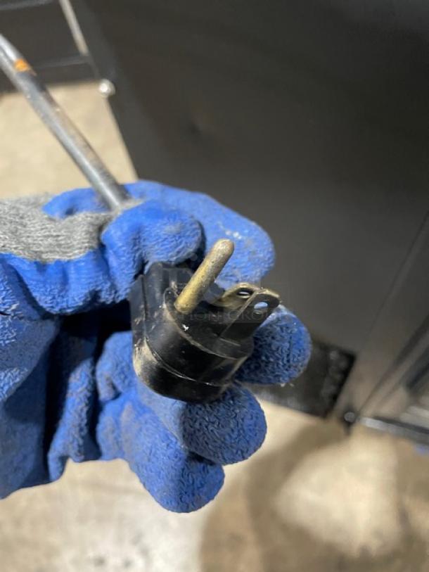 Power plug of True Commercial Back Bar Refrigerator TBB-60G-SD shown. Black plug held by gloved hand.