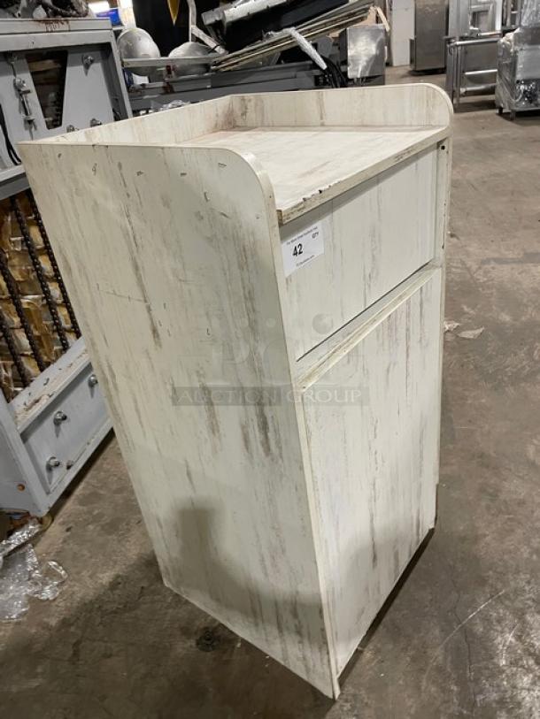 Commercial wooden enclosed-style trash cabinet, distressed white finish, standing in a warehouse. Marked with number 42.