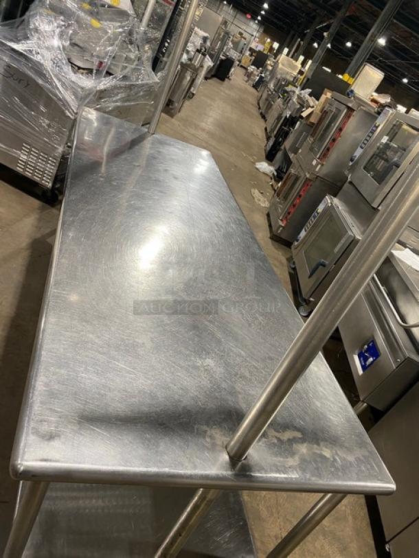 Commercial stainless steel worktop table with undershelf, overhead rack, and pull-out drawer. Mounted on sturdy legs.
