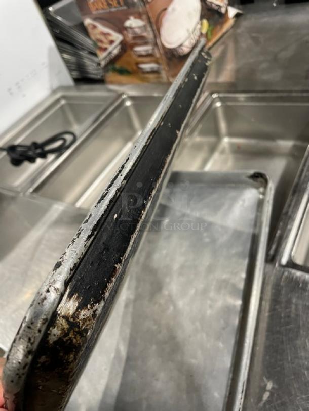 Worn commercial full-size sheet pan with visible scratches and discoloration, indicating heavy use.